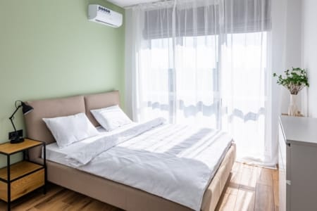Podwójne łóżko z szafką nocną i lampką przy oknie, mieszkanie w kompleksie Semitsvit