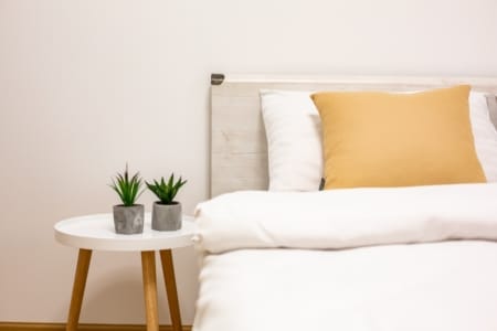 Bed with a yellow cushion and a side table with plants in the bedroom, Krakivska Street apartment