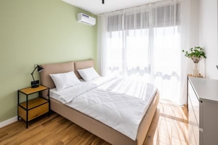 Jasna sypialnia z podwójnym łóżkiem i panoramicznym oknem w mieszkaniu w kompleksie Semitsvit