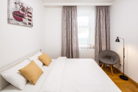 Bright bedroom with a bed, armchair and curtains in the Krakivska Street apartment