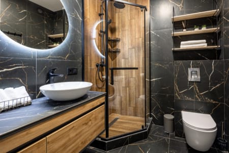 Bathroom with black marble, a vessel sink and a round mirror in the modern studio apartment in the Semytsvit complex