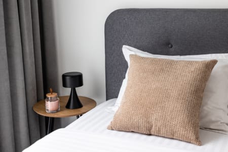 Bed with a beige cushion and a bedside table with a lamp, apartment in the Semytsvit complex