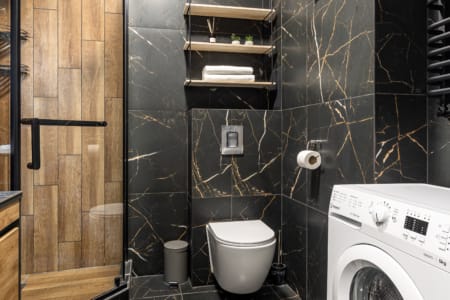 Bathroom with black marble-effect tiles and a washing machine in the modern apartment in the Semytsvit complex