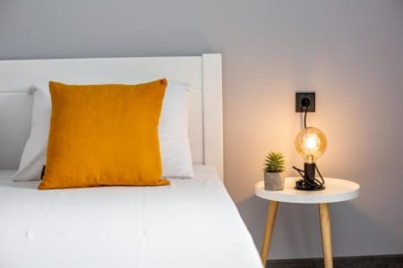 Łóżko z pomarańczową poduszką i lampka nocna w mieszkaniu przy ul. Listopadowego Czynu