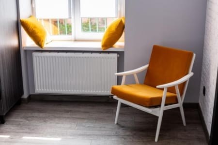 Fotel z pomarańczową poduszką przy oknie w mieszkaniu przy ul. Listopadowego Czynu