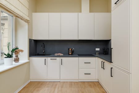 Kuchnia z kremowymi frontami i oknem w nowoczesnym apartamencie przy ul. Doroszenki