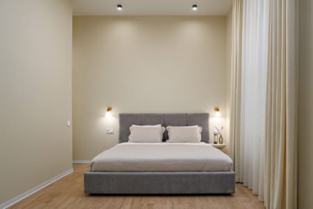 Podwójne łóżko z szarym wezgłowiem i kinkietami w nowoczesnym apartamencie przy ul. Doroszenki
