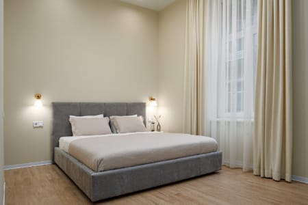 Sypialnia z dużym podwójnym łóżkiem i zasłonami w nowoczesnym apartamencie przy ul. Doroszenki