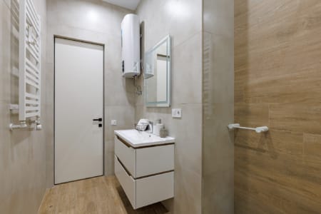 Łazienka z umywalką, bojlerem i płytkami imitującymi drewno w apartamencie przy ul. Doroszenki
