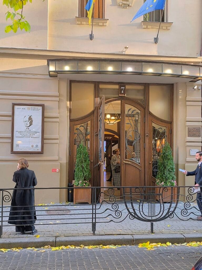 Вхід до філармонії | Leo Apartment Вхід до Львівської філармонії: дерев’яні двері з сецесійним декором і кована огорожа з лірою