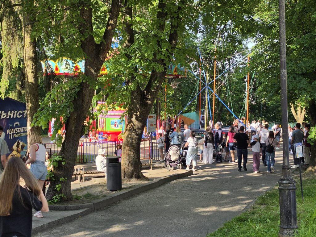Karuzele i trampoliny w Parku Kultury | Leo Apartment Karuzela łańcuchowa i trampoliny bungee wśród drzew w Parku Kultury we Lwowie