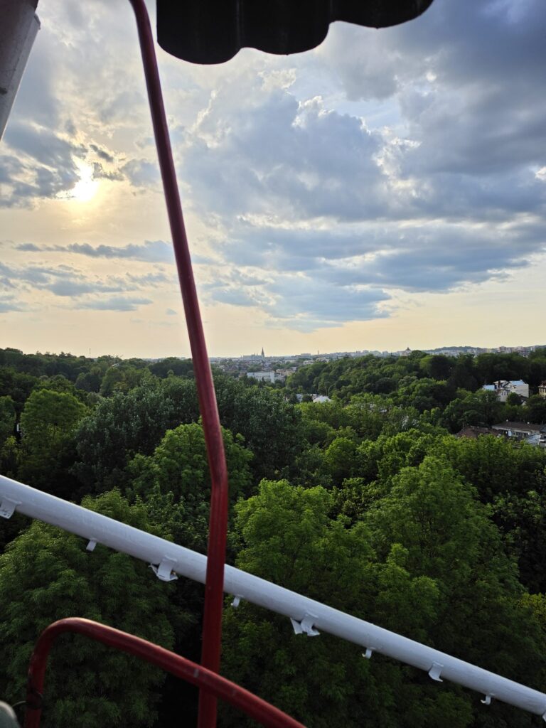 Widok z diabelskiego młyna w Parku Kultury | Leo Apartment Widok z gondoli diabelskiego młyna w Parku Kultury na zielone korony drzew i panoramę Lwowa