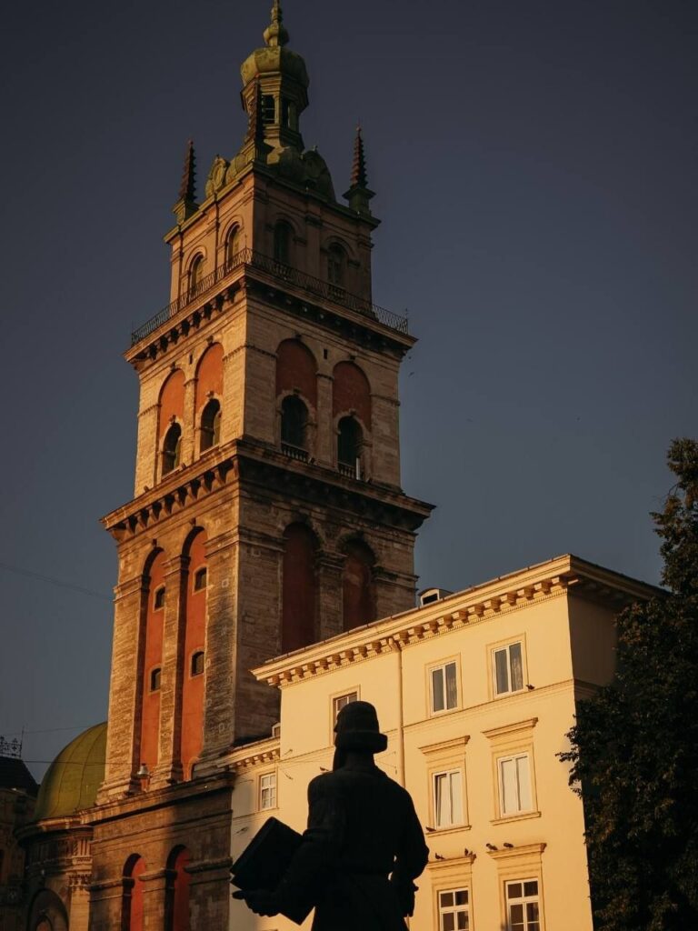 Вежа Корнякта у вечірньому світлі й силует пам’ятника Івану Федорову